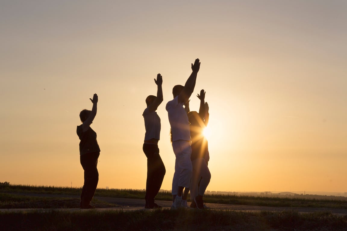 Group exercising Yoga outdoors at sunrise salutation to the sun